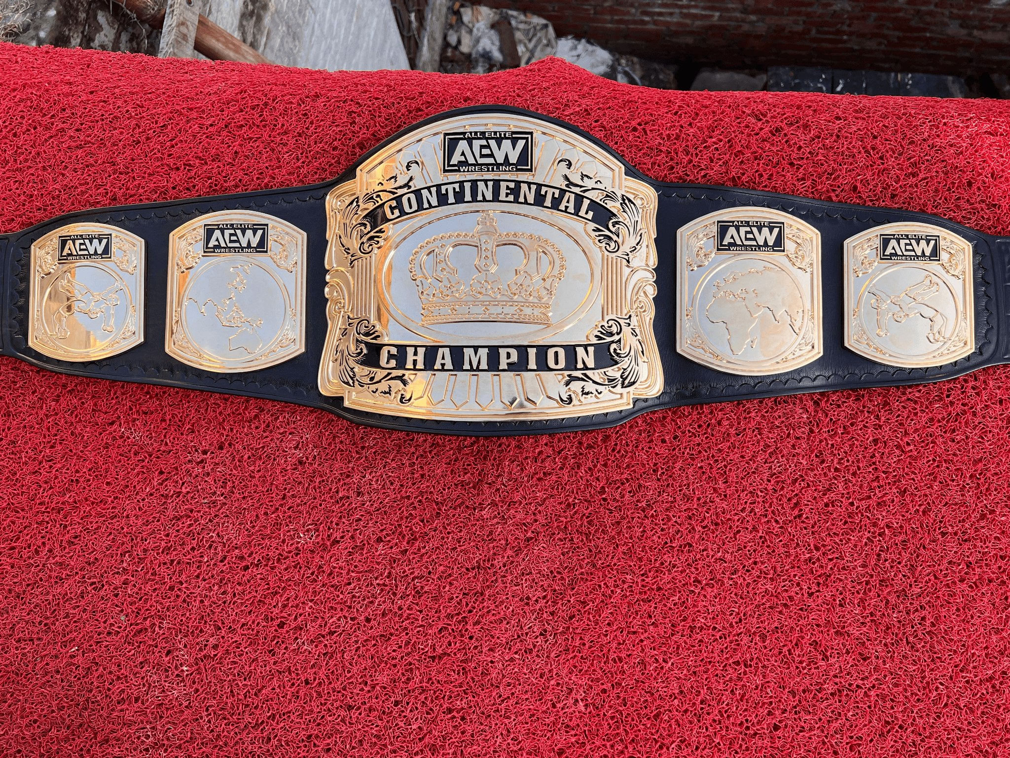 Continental Crown championship belt laid flat, showing the gold-plated crown centre plate and four side plates on a black leather strap